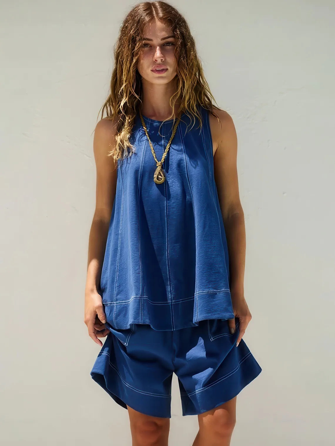 Woman wearing a blue sleeveless top and shorts against a plain background. #Color_DarkBlue