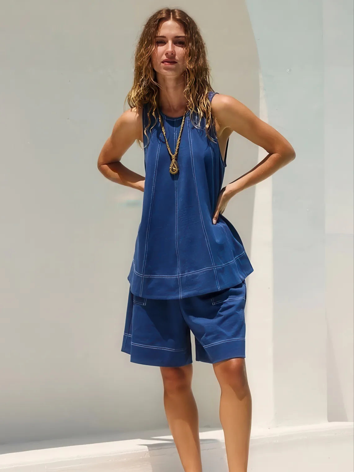 Woman wearing a blue sleeveless top and shorts against a white background. #Color_DarkBlue