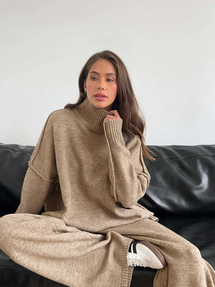 Woman wearing a beige sweater and pants sitting on a black leather couch. #Color_Tan