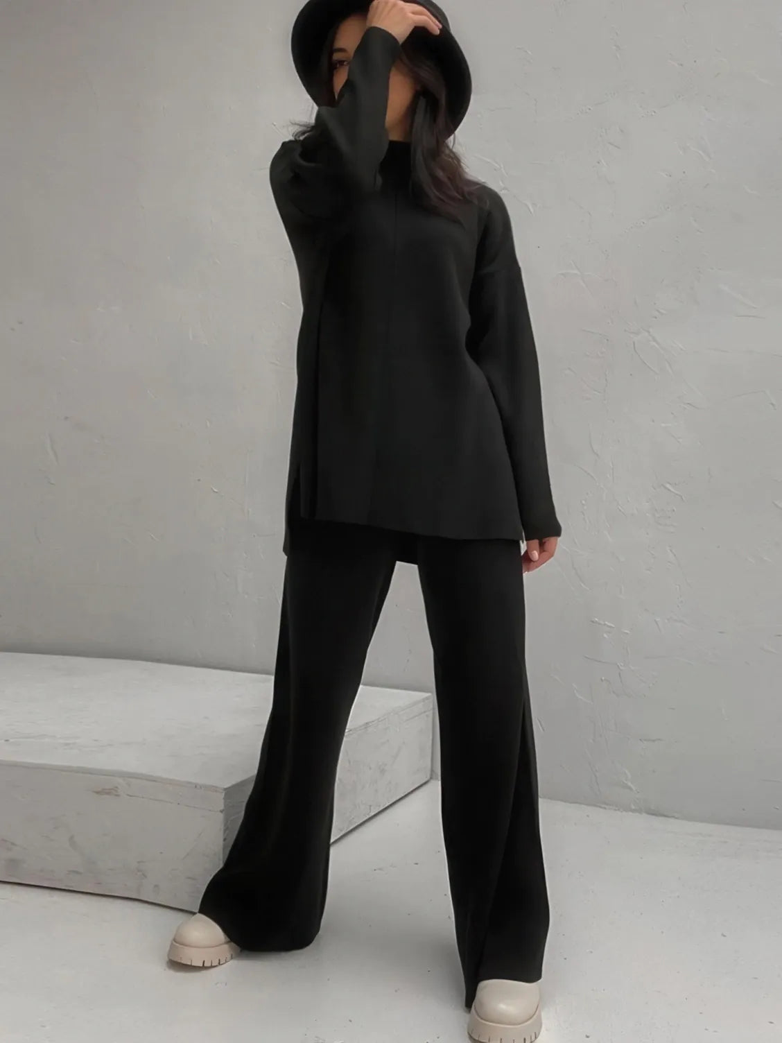 Person wearing a black outfit with wide-leg pants against a gray background. #Color_Black