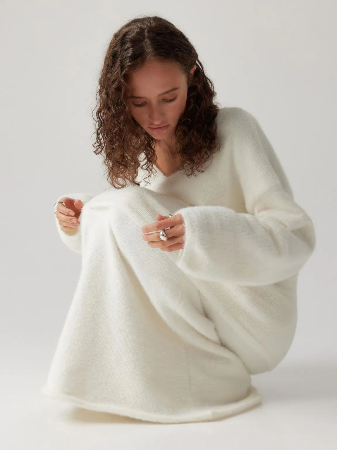 Woman wearing a white sweater against a plain background. #Color_White