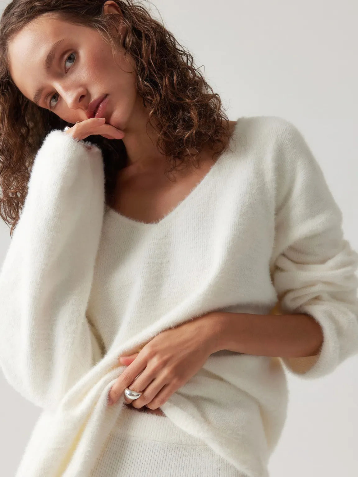 Woman wearing a white sweater against a plain background. #Color_White