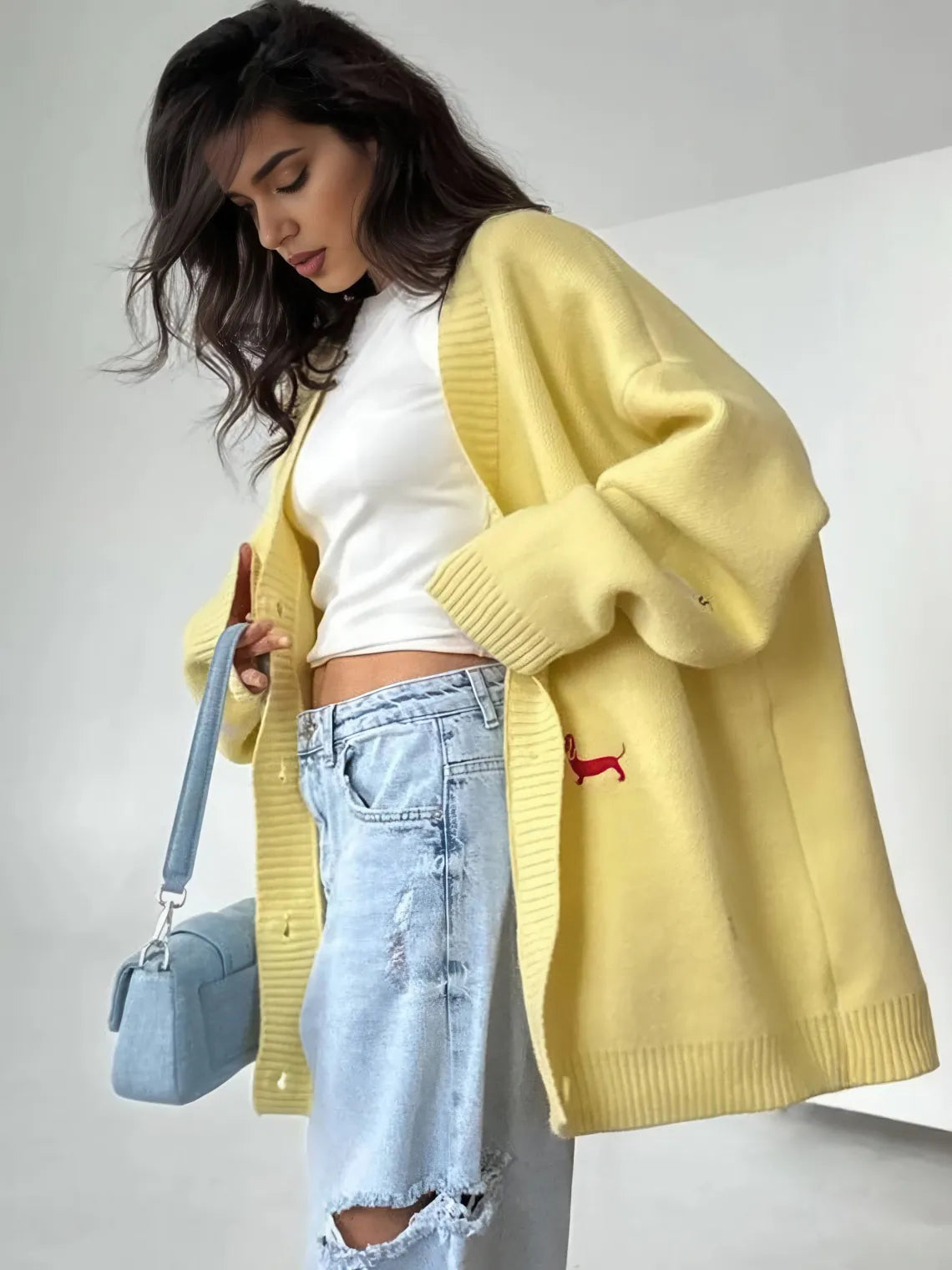 Woman wearing a yellow cardigan, white top, and ripped jeans, holding a blue handbag. #Color_Yellow