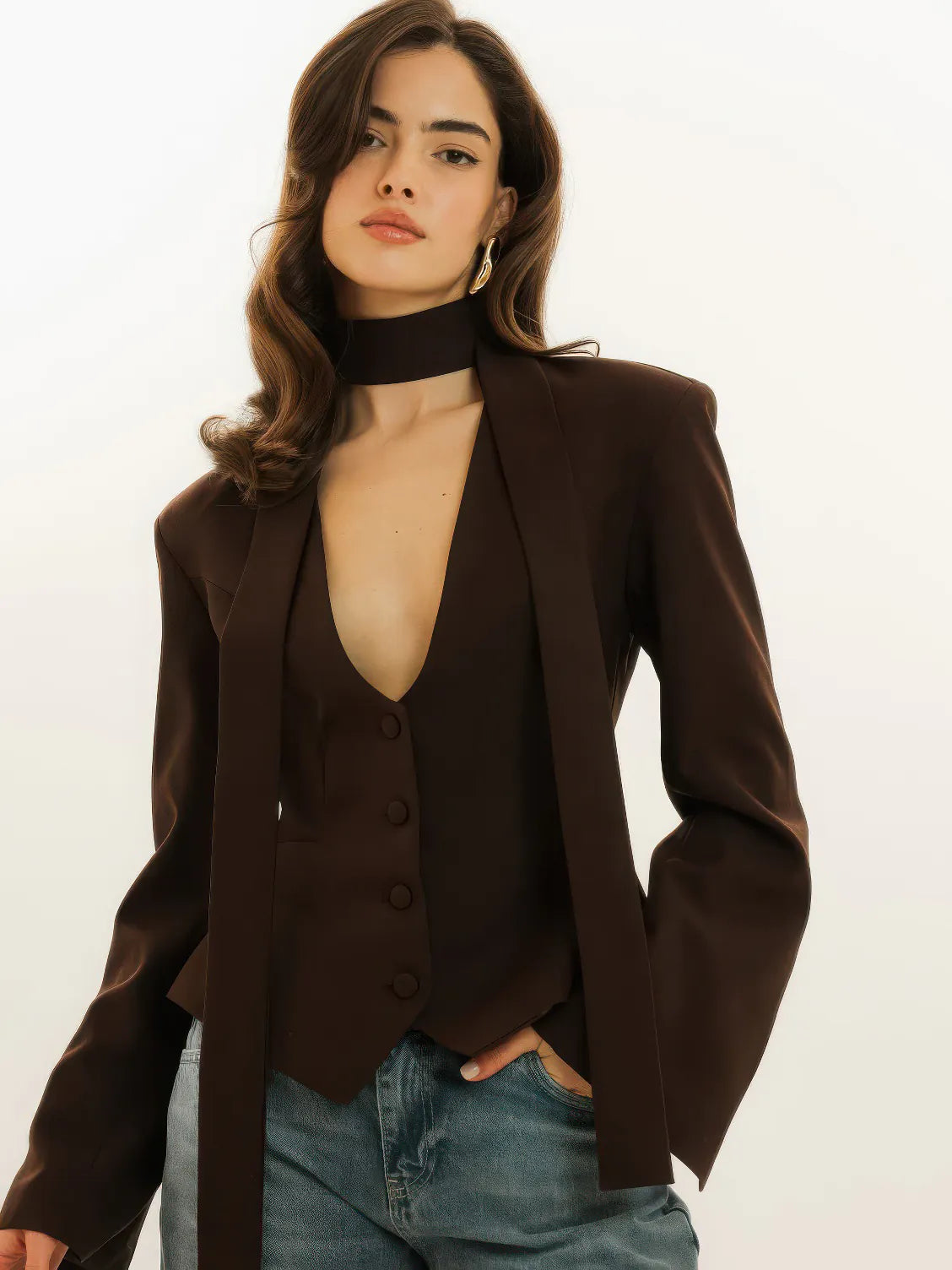 Woman wearing a brown blazer over a black top with blue jeans on a white background. #Color_Brown