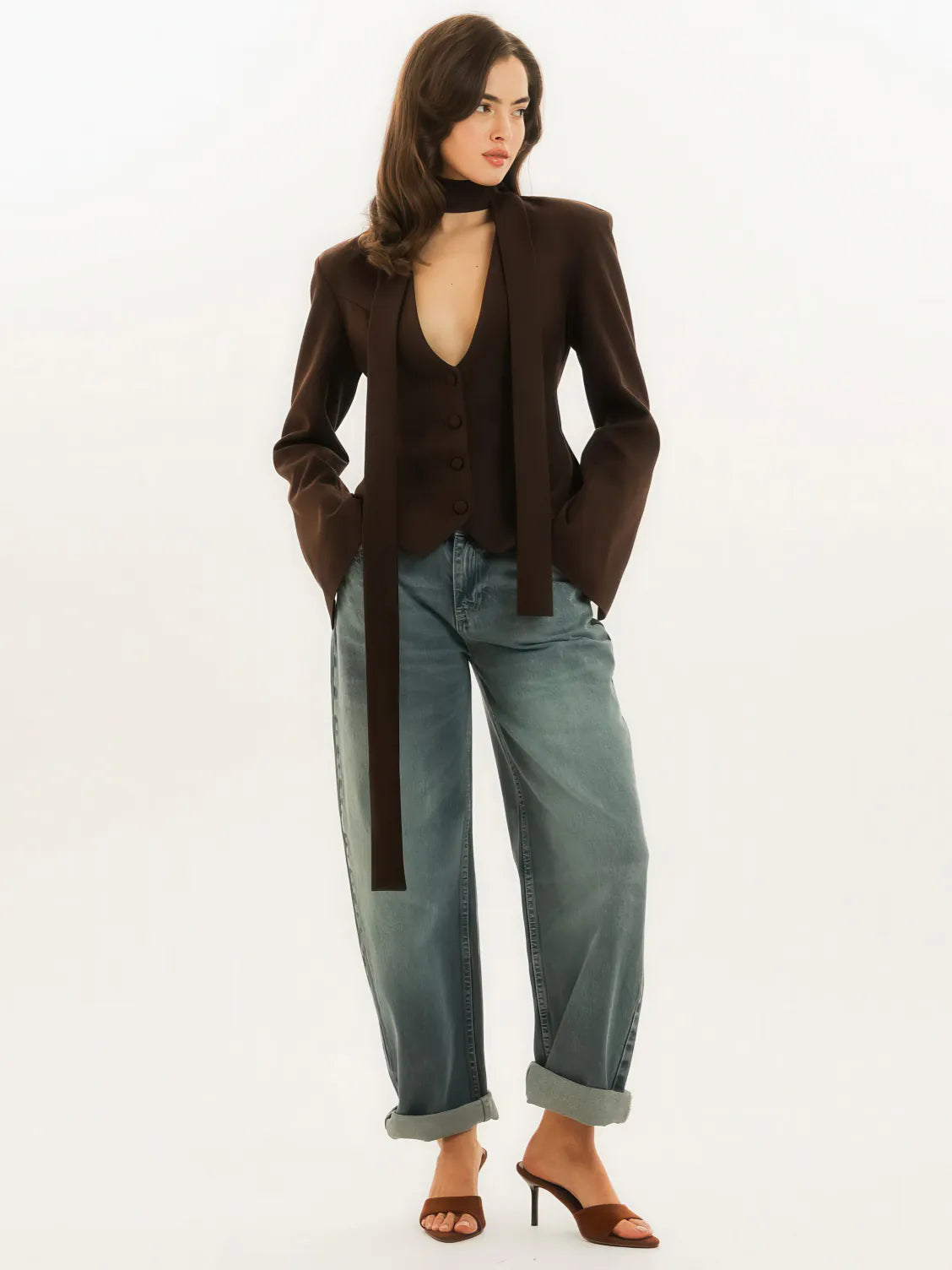 Woman wearing a brown blazer, black top, and blue jeans on a white background. #Color_Brown