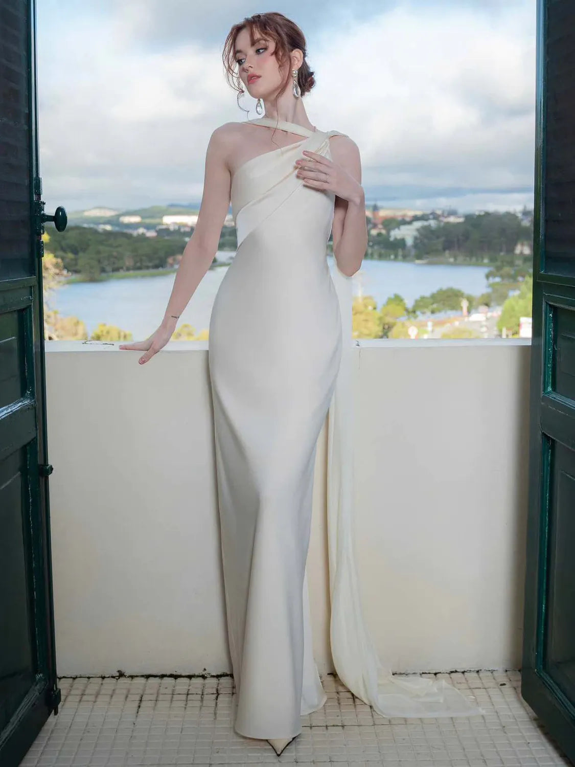 Woman in a white one-shoulder dress standing on a balcony with a scenic view. #Color_White