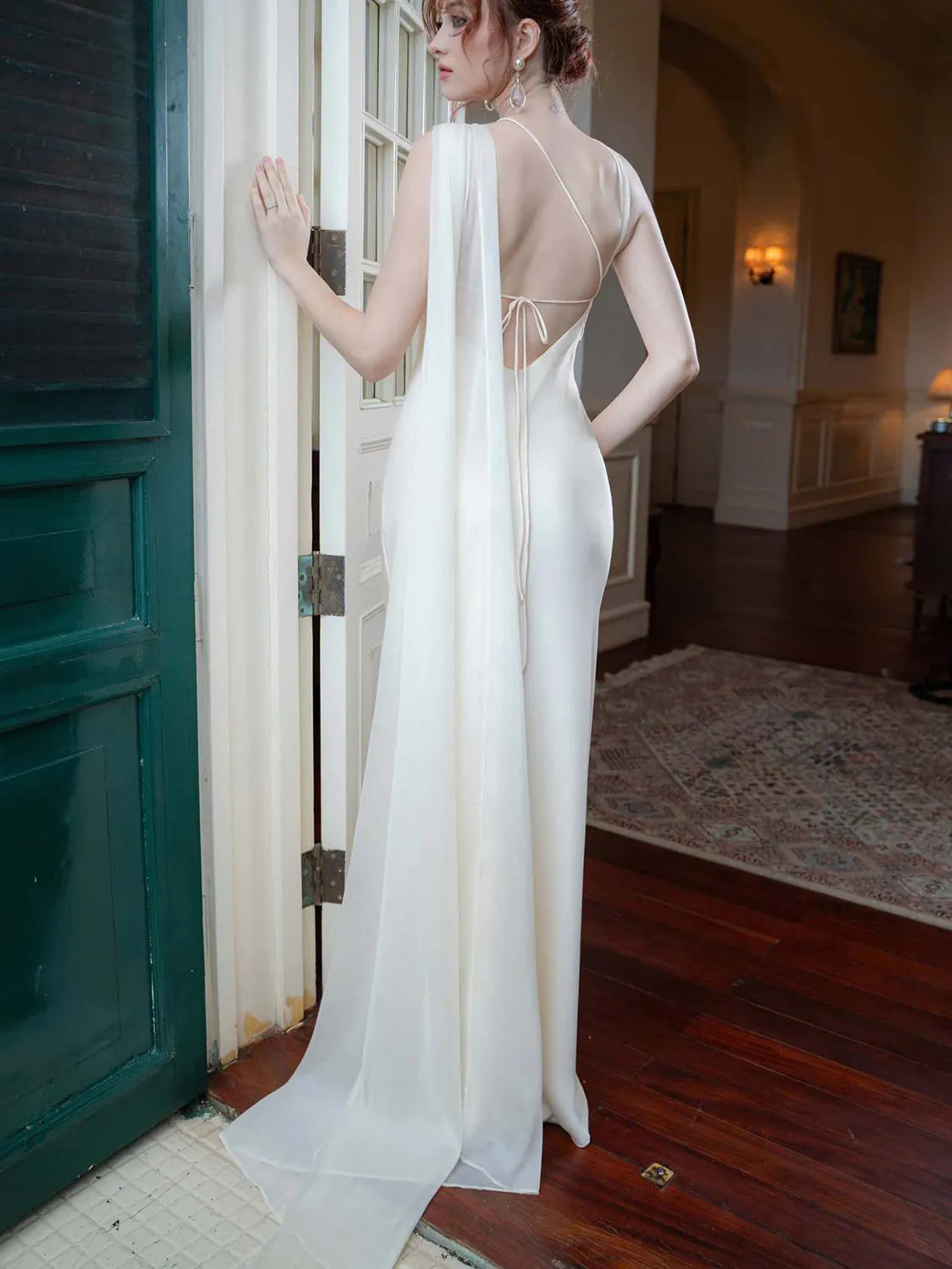 Woman in a white dress standing in a room with wooden floors and a green door. #Color_White