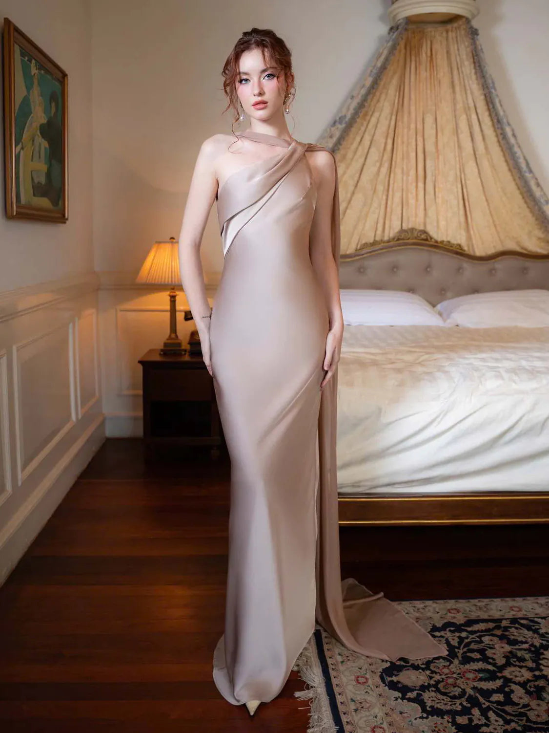 Woman in a elegant dress standing in a room with a bed and lamp. #Color_LightGray