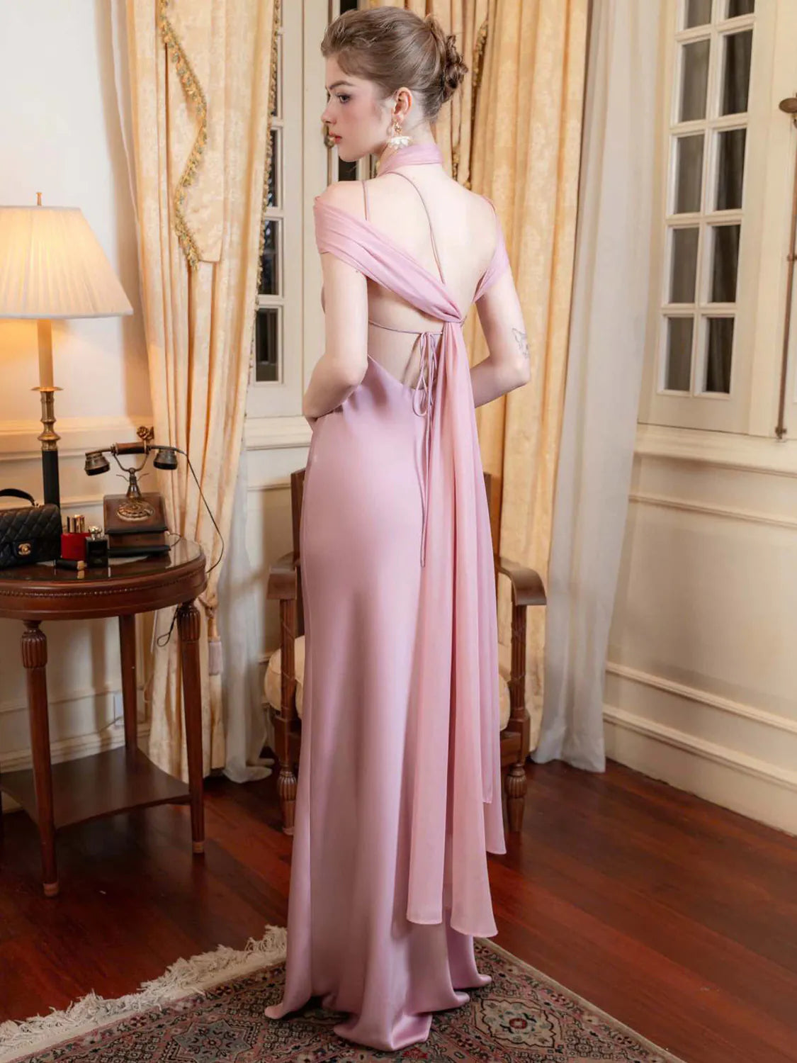 Woman in a pink evening gown standing in an elegant room with curtains and a table. #Color_Pink