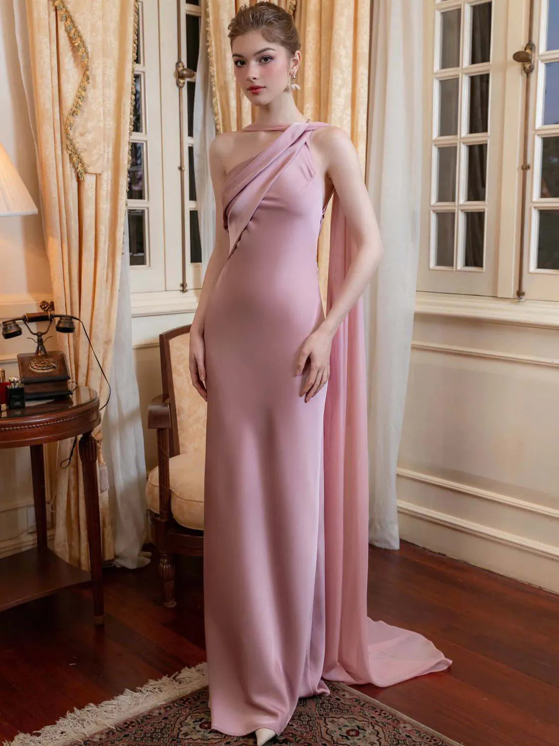 Woman in a pink evening gown standing in an elegant room with curtains and a table. #Color_Pink
