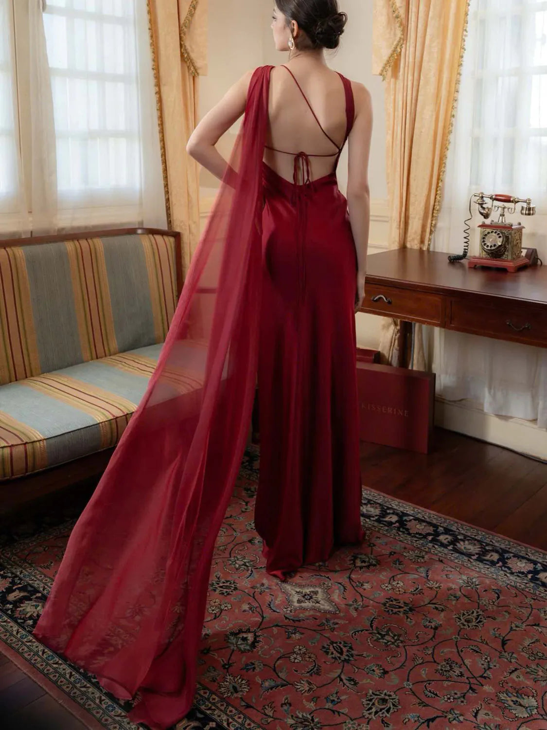 Woman in a red dress standing in a room with a couch and desk. #Color_Red