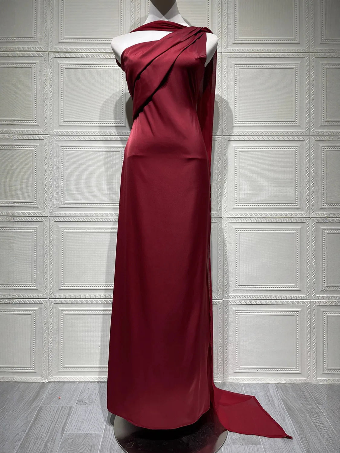 Red evening gown on a mannequin against a white paneled wall. #Color_Red