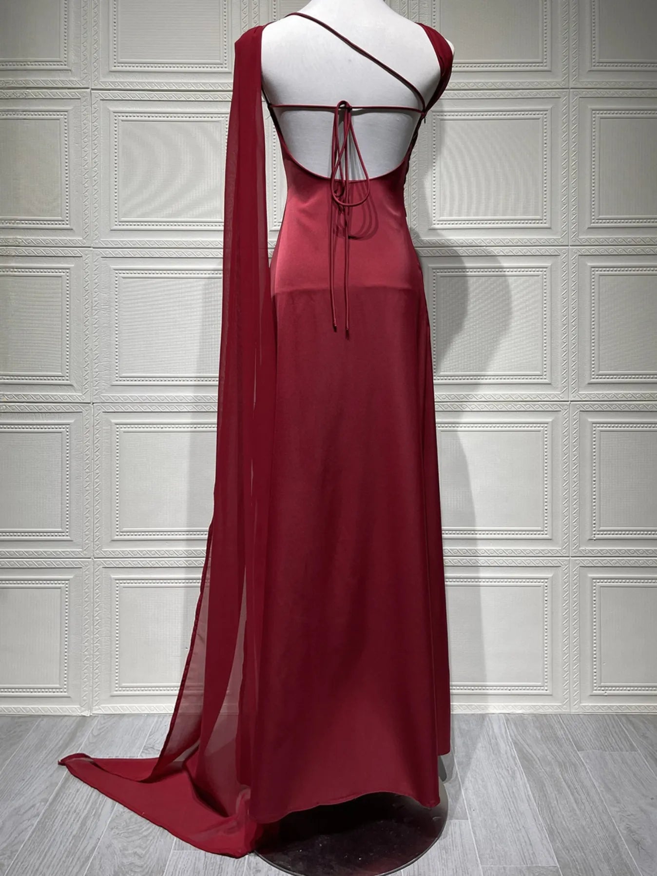 Red evening gown on a mannequin against a white paneled wall. #Color_Red